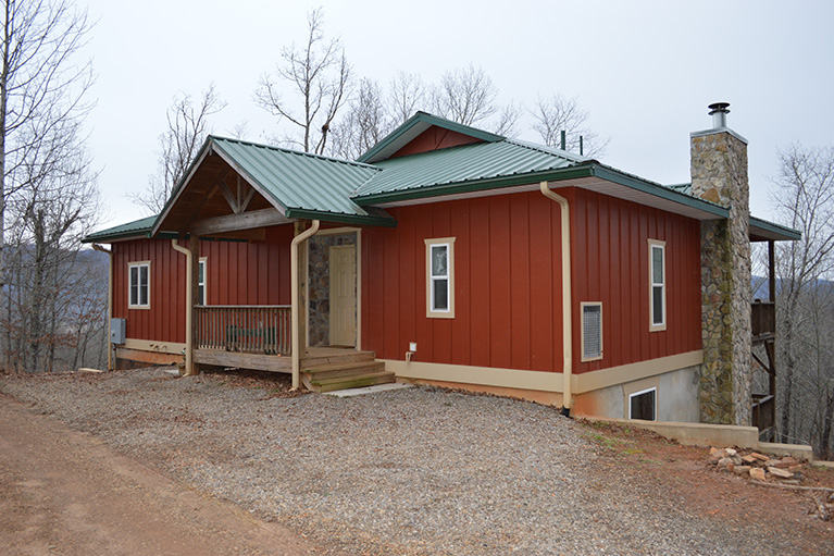 A red house with green roof and gravel driveway.