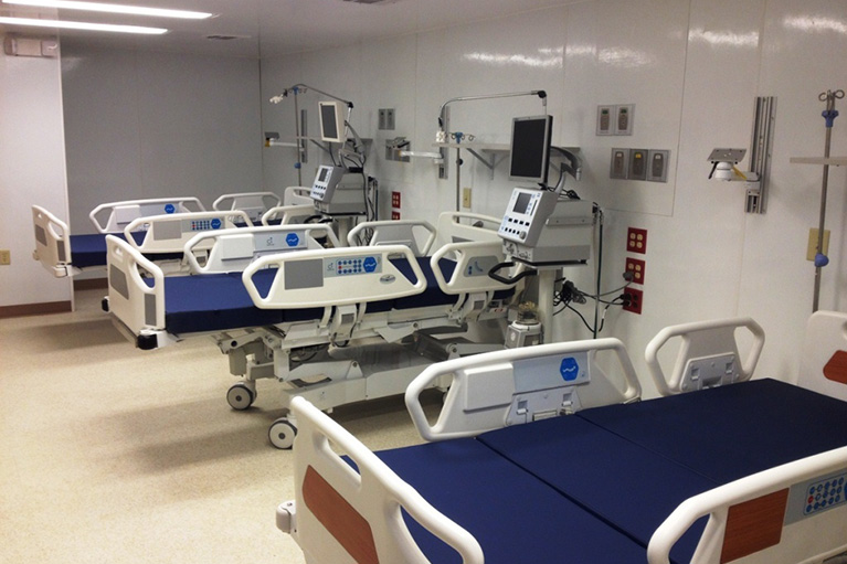 A hospital room with several beds and monitors.