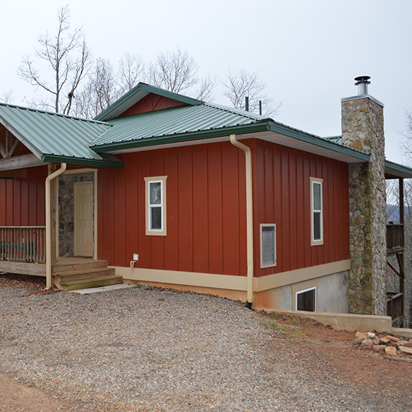 A red house with green roof and stone driveway.
