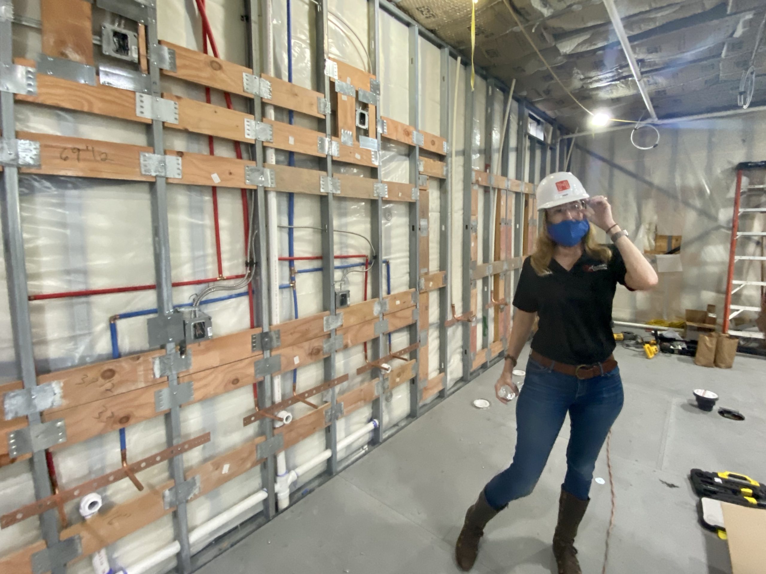 A woman wearing a hard hat and boots in front of a wall.